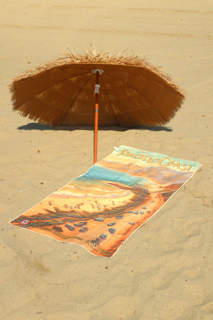 Pacific Coast vintage travel poster beach towel on the beach under a tiki umbrella