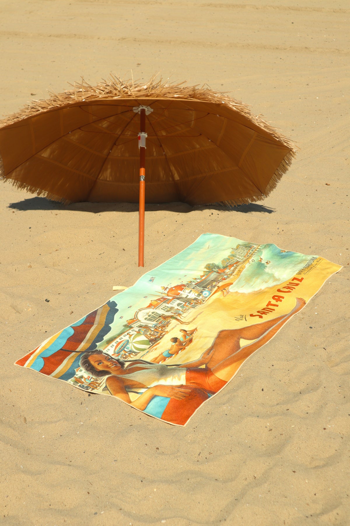 Santa Cruz vintage travel poster beach towel on sand under tiki umbrella