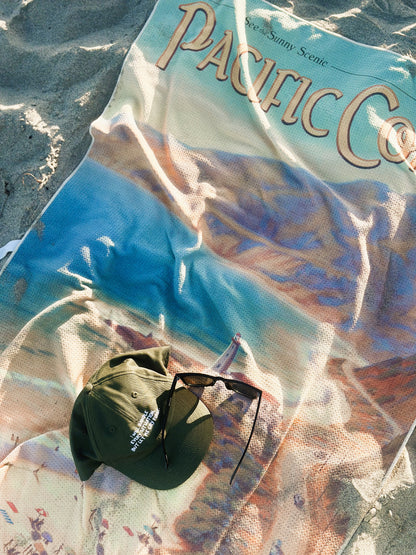 Pacific Coast vintage travel poster beach towel laying in sand with hat and glasses
